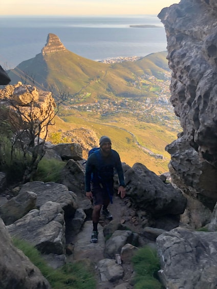 A hiker on a rocky trail with a view of a coastal town and mountains in the background. 3