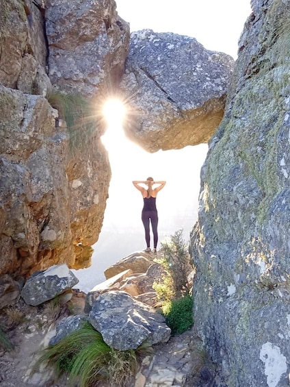 A person standing in a rocky landscape with a large rock arch formation. 1