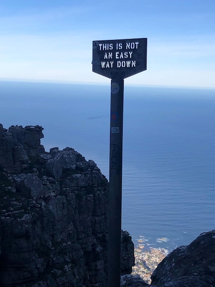 A signpost with a warning message against a backdrop of a rocky cliff and the ocean. 5