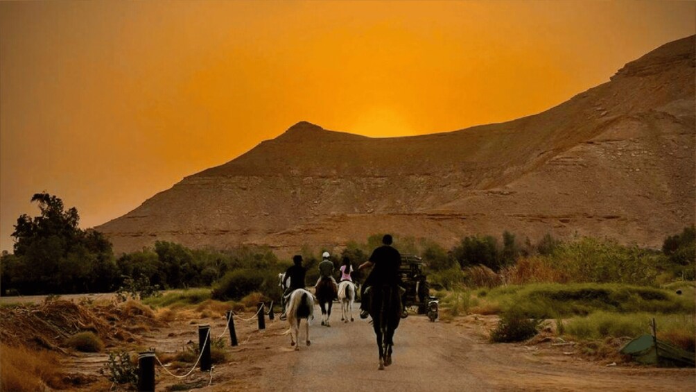 A group of people riding horses on a dirt road with a mountain in the background. 2