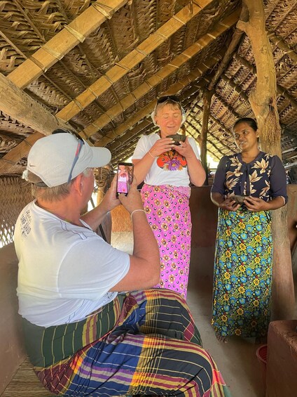 A person taking a photo of another individual in a traditional setting with a woven roof structure. 5