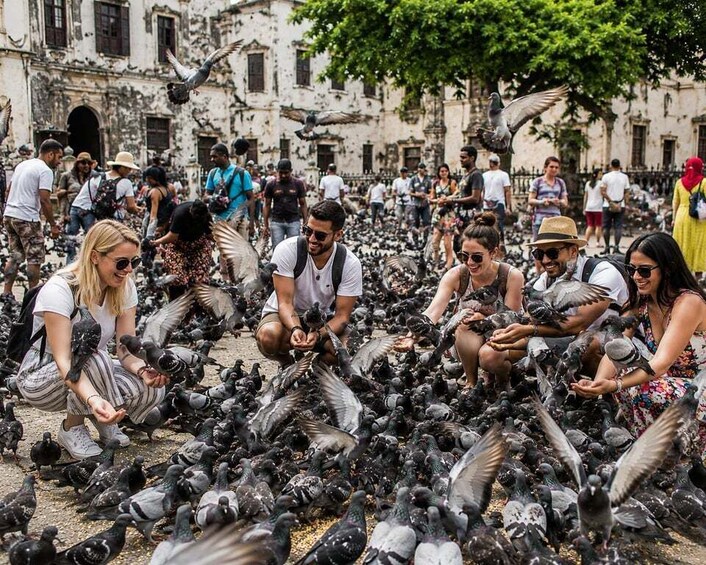 A group of people feeding pigeons in an urban setting with historic buildings in the background. 3