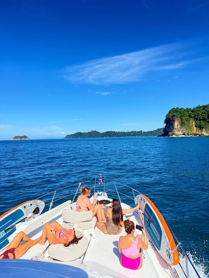 A boat with people relaxing on the deck, surrounded by a clear blue sea and a coastline with cliffs. 5