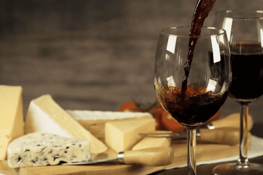 A glass of red wine being poured, cheese, and a knife on a wooden board. 3