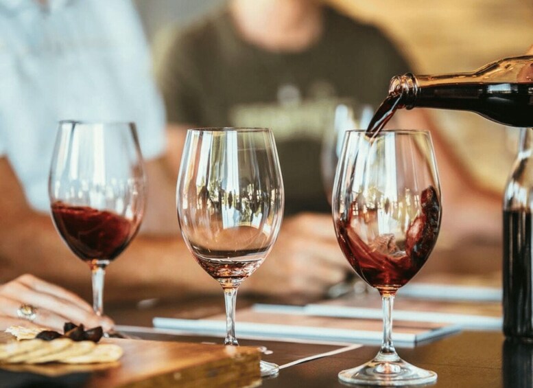 Three wine glasses on a table with a bottle pouring wine into one of them. 2