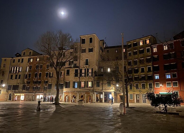 A nighttime urban square with illuminated buildings and a full moon. 5
