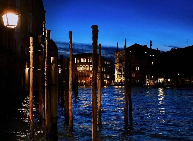 A canal with wooden poles and buildings with illuminated windows at dusk. 1