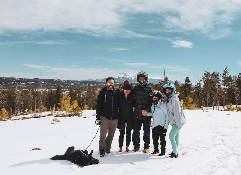 A group of people on a snowy mountain with a dog, wearing winter clothing and helmets. 5