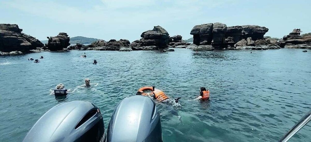 People swimming in a body of water with rocky formations in the background. 2