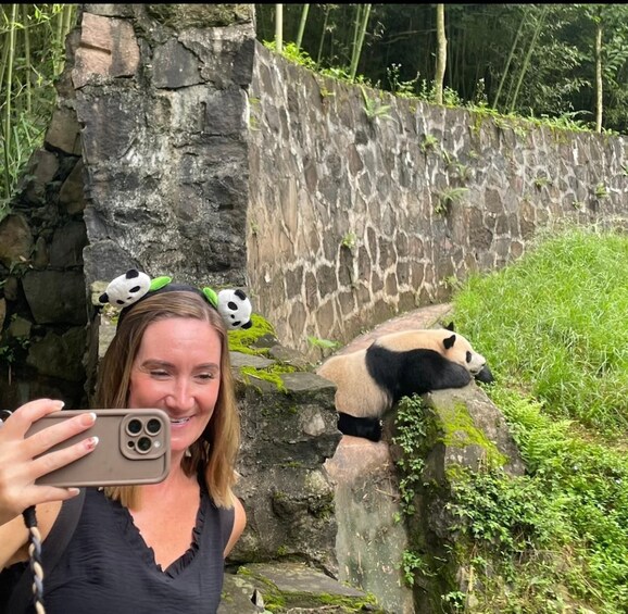 En person som tar en selfie med en panda i en inhägnad på en djurpark. 2