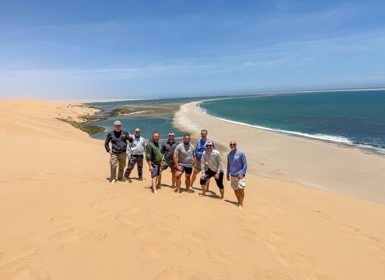 A group of people standing on a sandy beach with a clear view of the ocean and a distant shoreline. 4