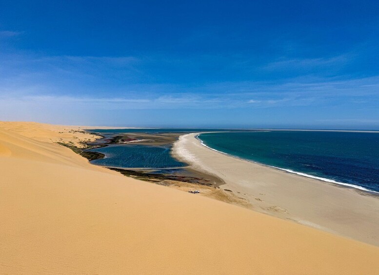 A coastal landscape with sand dunes, a beach, and a calm sea under a clear sky. 5