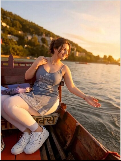 A person sitting on a wooden boat with a water body and a hilly landscape in the background. 1