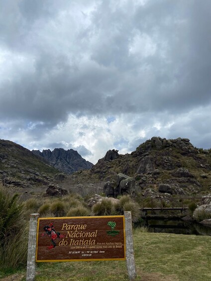 A sign for Parque Nacional do Itatiaia with a mountainous landscape in the background. 1