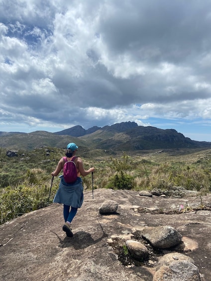 A hiker with a backpack and walking sticks on a rocky terrain with mountains in the background. 2