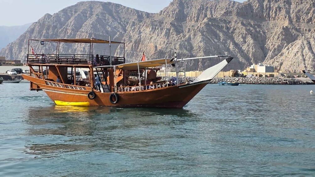 A wooden boat with a cabin and passengers, docked near rocky mountains. 4