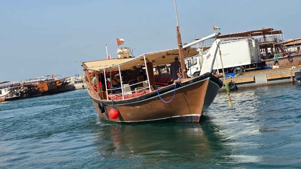 A wooden boat docked at a harbor with a crane and other boats in the background. 3