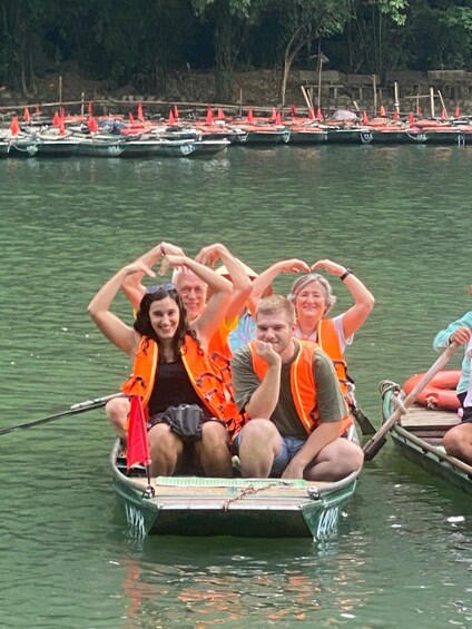 Eine Gruppe von Personen in einem Ruderboot auf ruhigem Gewässer, gekleidet in orangefarbene Schwimmwesten. 3