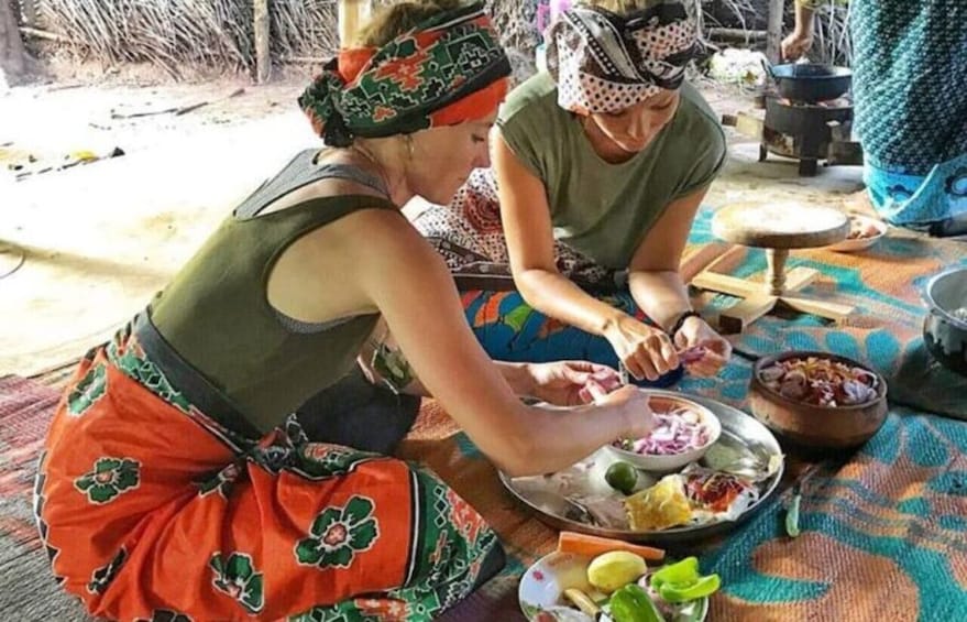 Two individuals preparing food outdoors with a variety of dishes and cooking utensils on a mat. 5