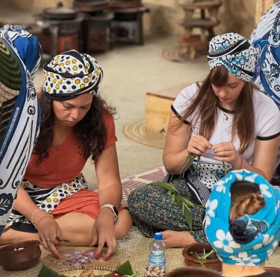 Two women sitting on the floor, engaged in a craft activity with materials like leaves and a bowl. 1