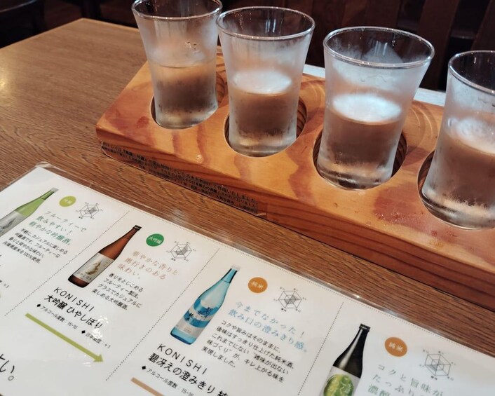 A wooden tray with four glasses of a frothy beverage, likely beer, and a menu with drink descriptions in Japanese. 5