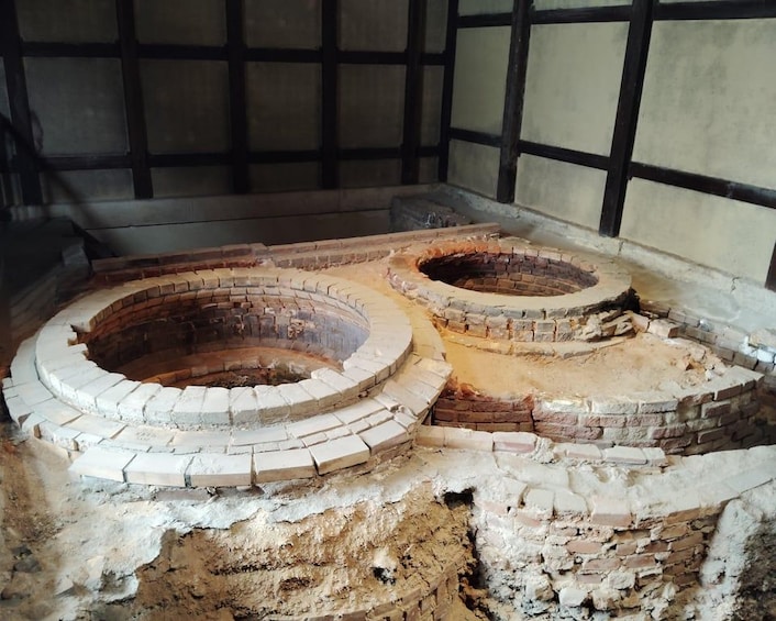An ancient stone structure with circular openings, possibly a historical well or oven, surrounded by a brick wall. 2