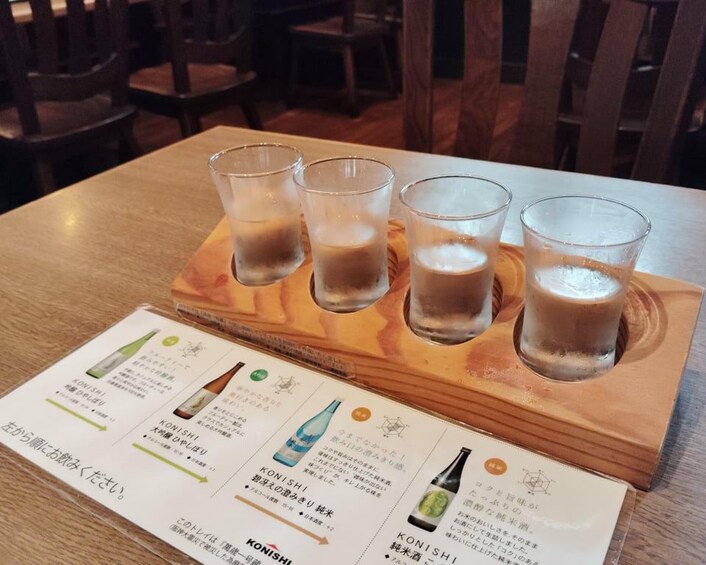 A wooden tray with four glasses of a beverage, a menu with drink options, and a restaurant setting. 4
