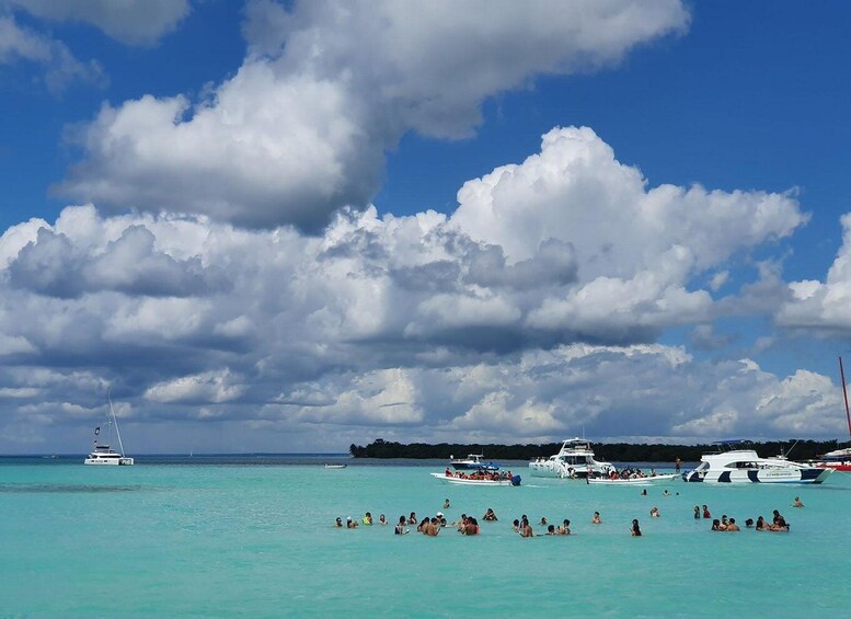 A tropical beach with turquoise water, a sailboat, and several yachts. 1