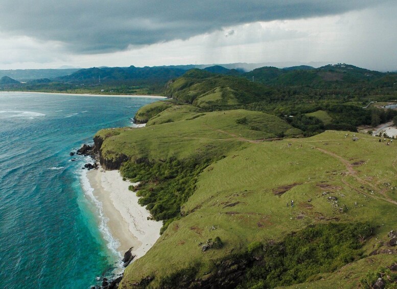 A coastal landscape with a beach, grassy hills, and a cloudy sky. 5