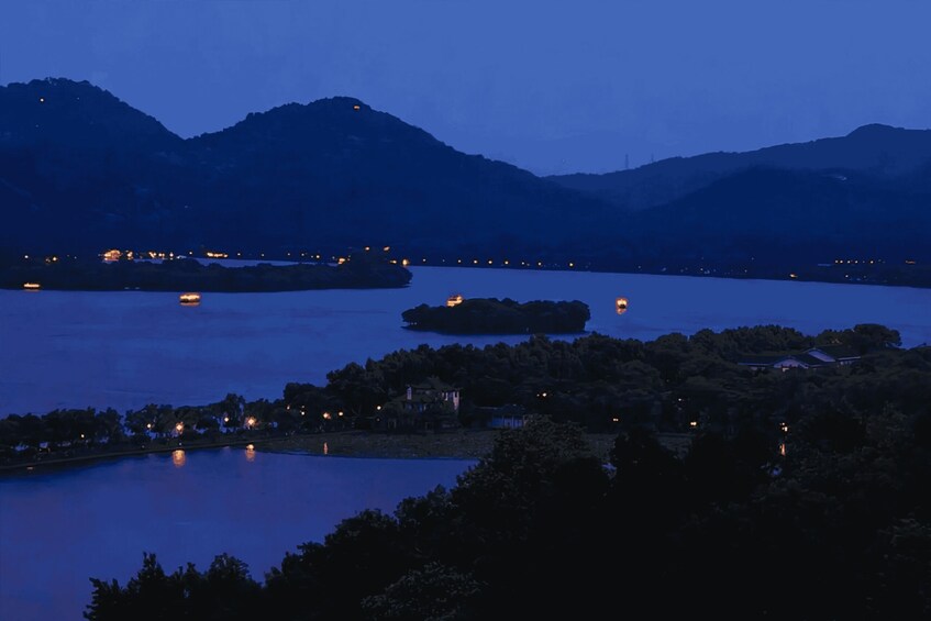 A lake at dusk with mountains in the background and small lights on the shore. 4