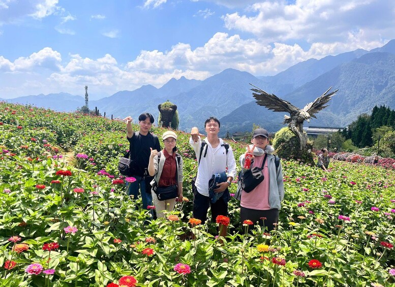 A group of people standing in a flower field with mountains in the background. 2