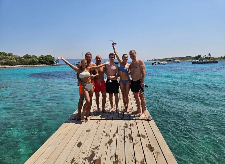A group of people on a wooden pier extending into clear turquoise water, with boats and greenery in the background. 5