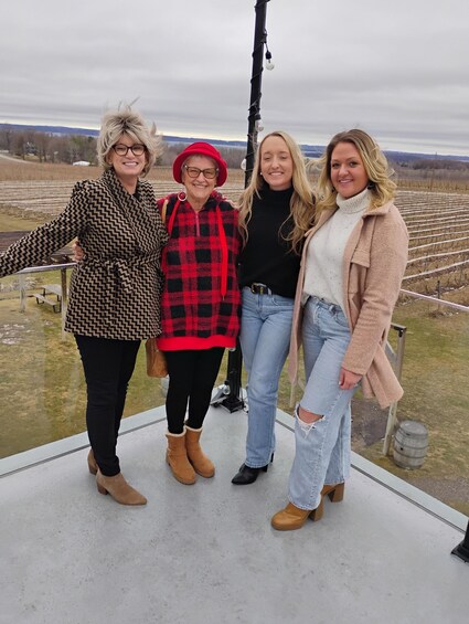 Four people standing on a platform with a vineyard in the background. 4