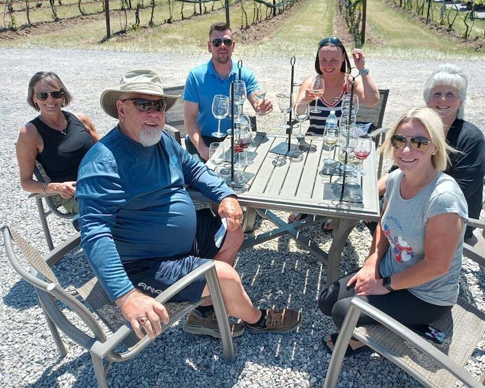 A group of people seated around a table with wine glasses, in a vineyard setting. 2