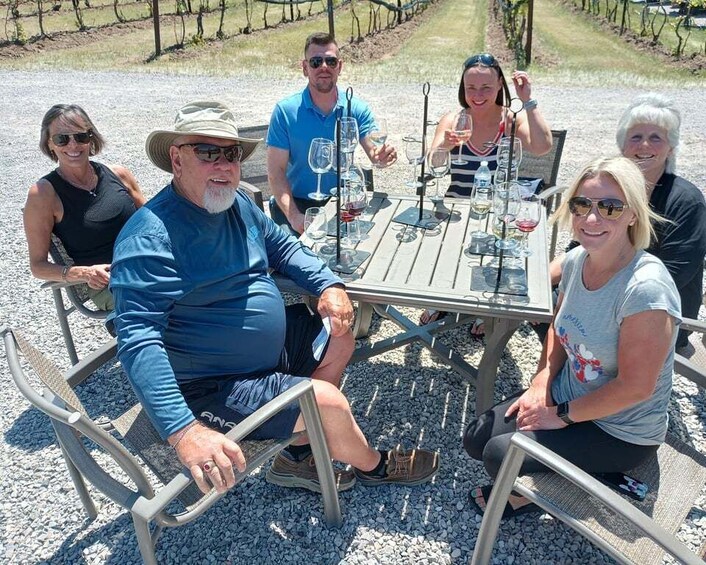 A group of people seated at a table outdoors with wine glasses and bottles. 2