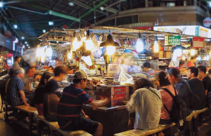 A bustling food market with people dining at tables and a food stall in the center. 1