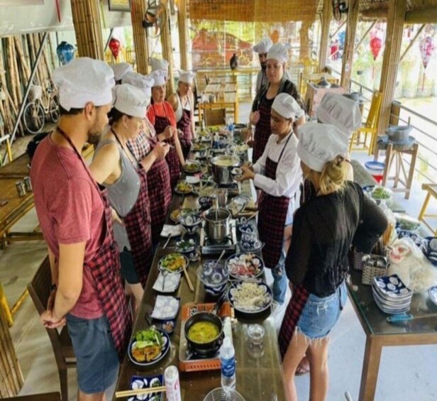 A group of people in chef hats and aprons preparing food at a long table with various dishes and cooking utensils. 5