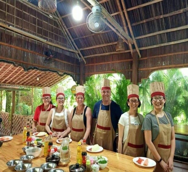 A group of people in aprons and chef hats standing around a table with cooking ingredients and utensils. 4