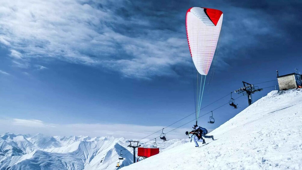 A person kiteboarding on a snowy mountain slope with ski lifts in the background. 3