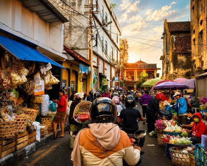 A bustling street market with vendors and shoppers, surrounded by buildings with signs and awnings. 2