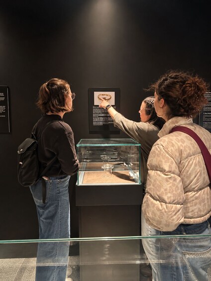 Two people examining an exhibit with a glass display case containing a golden object and informational plaques. 1