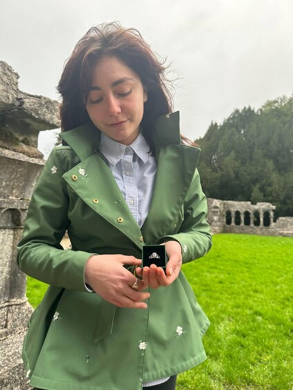 A person holding a ring box outdoors near ancient ruins. 1