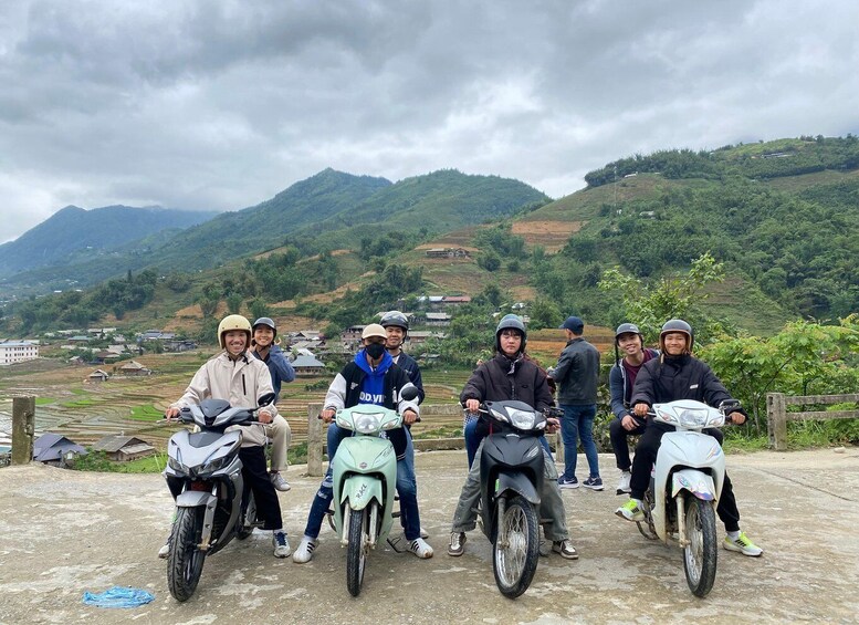 A group of people on motorcycles in a rural area with terraced fields and mountains in the background. 1