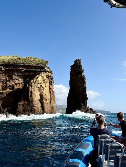 A boat with passengers taking photos of a coastal rock formation. 1