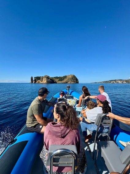 A group of people on a blue boat with rocky cliffs in the background. 2