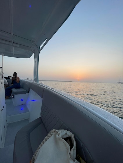 A boat interior with a person sitting on the deck, a dog, and a sunset in the background. 3