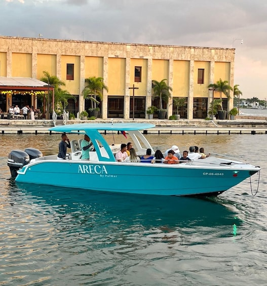 A turquoise boat named ARECA by Palmar on calm waters near a building with palm trees. 1