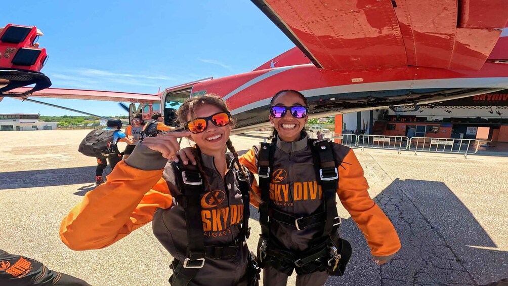 Two people in skydiving gear standing in front of a red aircraft. 2