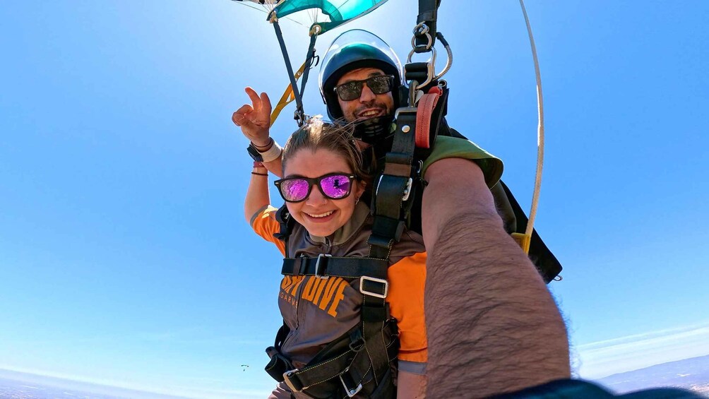 A person skydiving with another individual, both wearing parachutes and safety gear. 3