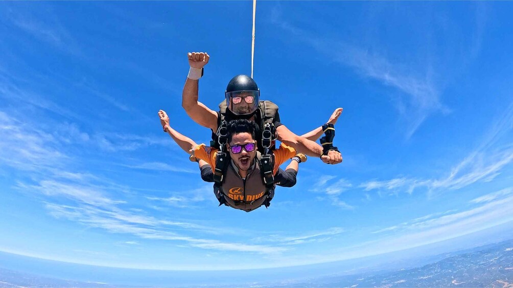 Two people skydiving with parachutes against a clear blue sky. 5